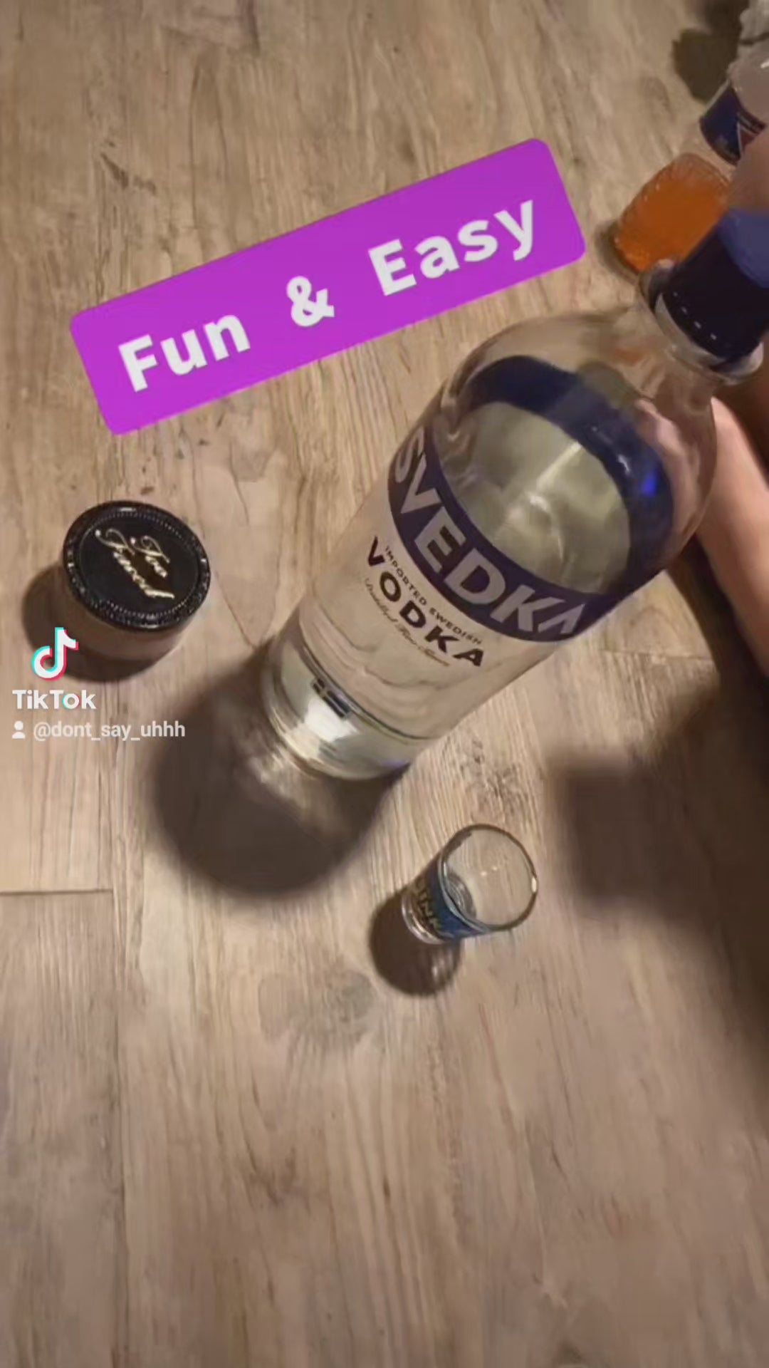 Load video: In a lively party setting, friends gather around a table, pouring shots of vodka into shot glasses with excitement. The camera then zooms in on a game box labeled &#39;Don&#39;t Say Uhhh,&#39; indicating the start of a drinking game.